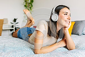 Young pretty woman listening music with wireless headphones while lying on bed