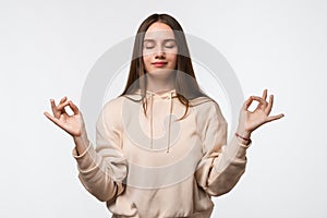 Young pretty woman with long chestnut hair straight hair keeps hands in mudra gesture, holds fingers in yoga sign