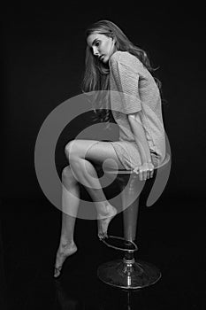 young pretty woman with long hair in dress posing on black background on stool