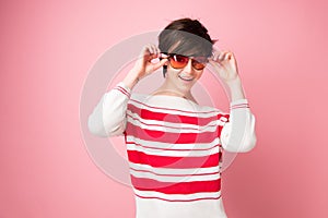 Young pretty woman looking at camera wearing sun glasses over pink background. Happiness, good mood, flirt, posing, femininity,