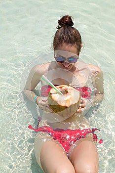 Young pretty woman lying in the sea with coconut