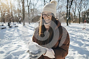 Young pretty woman making snowball outdoors in the park