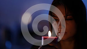 young pretty woman is making a wish holding burning candle, portrait in darkness