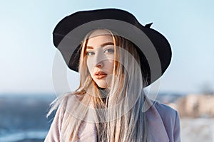 Young pretty woman with pale skin with beautiful make-up with brown eyes, with blond hair in an elegant hat in a pink coat