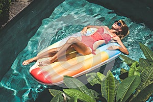 Young pretty woman with perfect tanned body lying on air mattress in the pool in summer and having fun. Relaxing