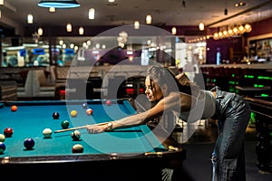 young pretty woman playing alone snooker holding cue at pool table