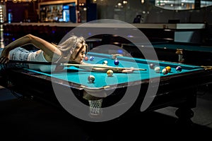 young pretty woman playing alone snooker holding cue at pool table