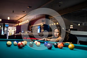 young pretty woman playing alone snooker holding cue at pool table
