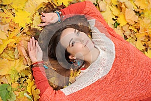 Young pretty woman portrait, laying in autumn leaves, dressed in fashion orange sweater