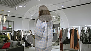 Young pretty woman is posing in a long fur coat at clothing store, tracking shot, 360 degree