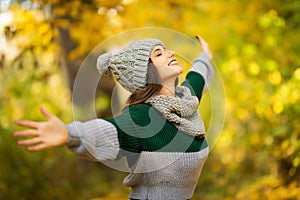 Young woman with raised hands enjoy autumn sunny weather in park