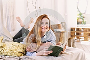 Young pretty woman is reading a book at home in bed. House reading concept, bright interior