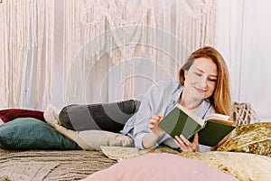 Young pretty woman is reading a book at home in bed. House reading concept, bright interior