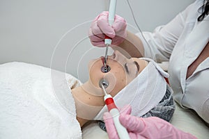 Young pretty woman receiving facial performing microcurrent stimulation treatment at spa clinic