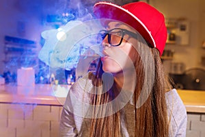 Young pretty woman in red cap smoke an electronic cigarette at the vape shop