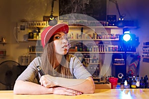 Young pretty woman in red cap smoke an electronic cigarette at the vape shop