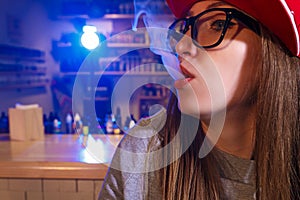 Young pretty woman in red cap smoke an electronic cigarette at the vape shop. Closeup.