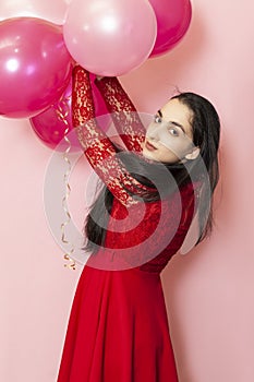 Young pretty woman in red evening dress holding festive air balloons. Portrait of happy 20s middle-eastern female celebrating