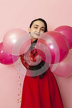 Young pretty woman in red evening dress holding festive air balloons. Portrait of happy 20s middle-eastern female celebrating