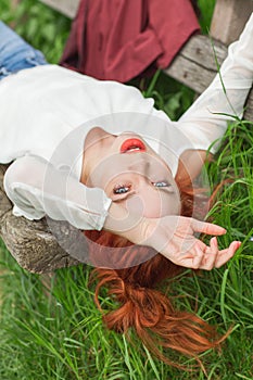 Young pretty woman with red hair lying on garden bench relaxing