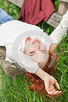 Young pretty woman with red hair lying on garden bench relaxing