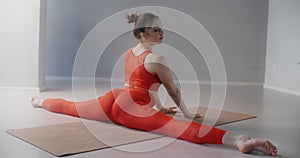 Young pretty woman in red sports tracksuit sits on the twine and demonstrates stretching and yoga exercises in slow