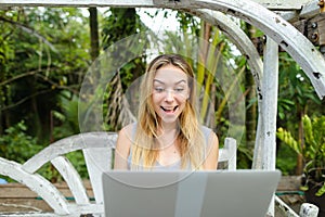 Young pretty woman resting on swing and using laptop, palms in background.