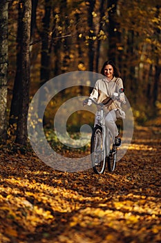 Young pretty woman riding vintage white bicycle in autumn park. Lady having fun on orange nature fall background.