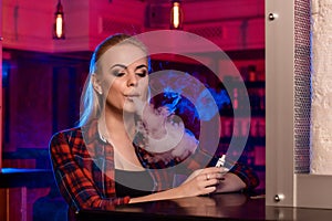 Young pretty woman in a shirt in a cage smoke an electronic cigarette at the vape bar