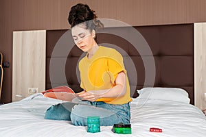 A young pretty woman sitting on the bed and reading a magazine. Home. Reading and education