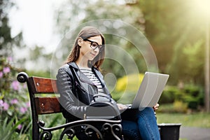 Young pretty woman sitting on bench in the park, using laptop computer, networking online on wireless. Student work on laptop in p