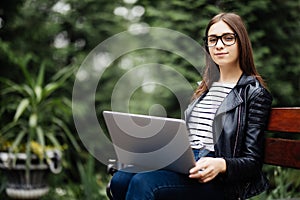 Young pretty woman sitting on bench in the park, using laptop computer, networking online on wireless. Student work on laptop in p