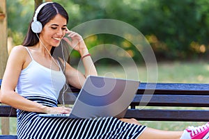 Young pretty woman sitting on bench in the park, using laptop computer