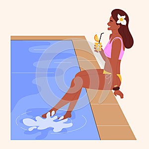 Young pretty woman sitting at the edge of a swimming pool, sunbathing and drinking cocktail