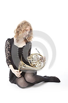 Young pretty woman sitting and holding french horn