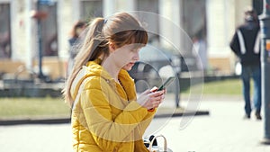 Young pretty woman sitting on a park bench browsing her smartphone outdoors on warm autumn day