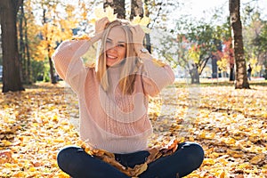 Young pretty woman is sitting on tground in autumn park with leaves in her hands