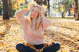 Young pretty woman is sitting on tground in autumn park with leaves in her hands