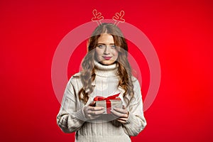 Young pretty woman smiling and holding gift box on red studio background.