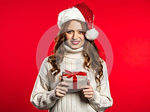 Young pretty woman smiling and holding gift box on red studio background.