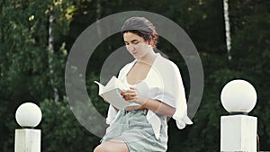 Young pretty woman smiling and reading book in green park