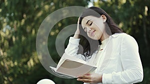 Young pretty woman smiling and reading book in green park