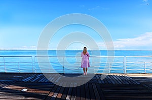 Young pretty woman standing alone on the pier near the sea