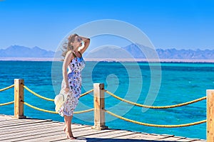 Young pretty woman standing alone on the pier near the sea and looking on the water and waiting for somebody in ocean