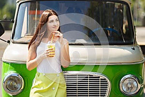 Young pretty woman standing near vintage van with glass of lemon
