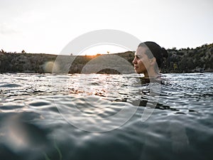 young pretty woman swimming in lake water on sunset