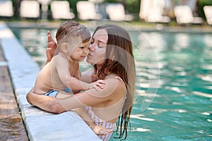 Young pretty woman in a swimming pool kissing her baby boy