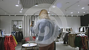 Young pretty woman is taking a photo of herself dressed in blue jacket at clothing shop, tracking shot, 360 degree