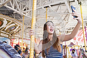 Young pretty woman taking selfie on carousel in amusement park. Attractive women taking selfie in amusement park