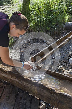 Young pretty woman taking water from mountain stream